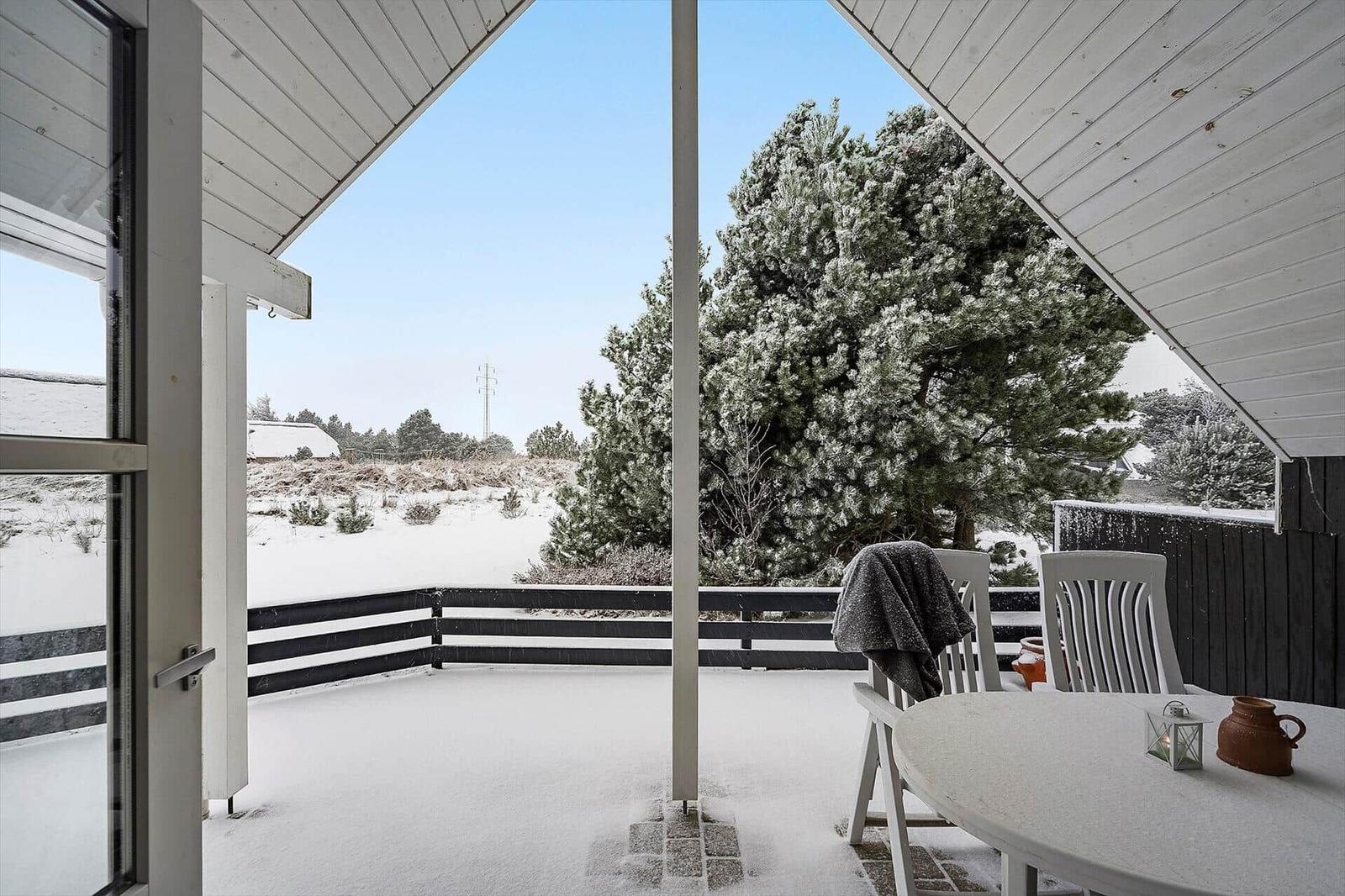 Terrasse mit Tisch und Stühlen, Schnee bedeckt den Boden und Bäume. Blick auf winterliches Landschaft.