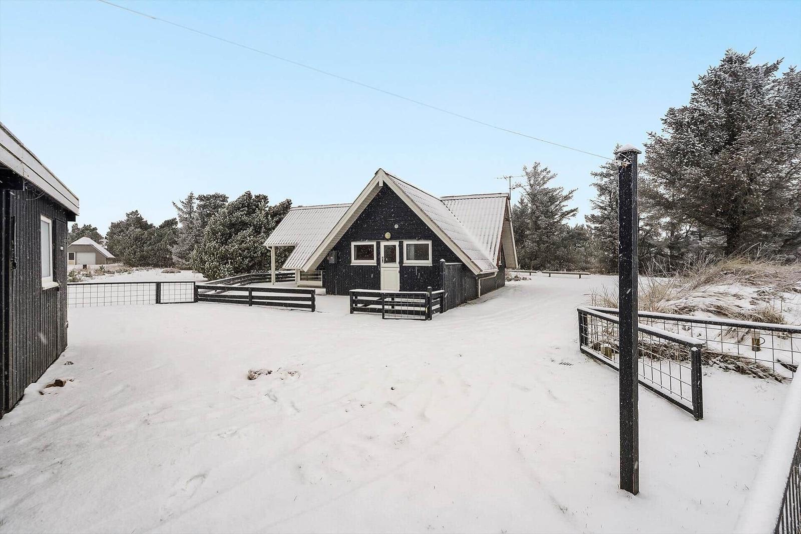 Schwarz gestrichenes Haus mit Schneebedecktem Dach und Gartenzaun im Winter.