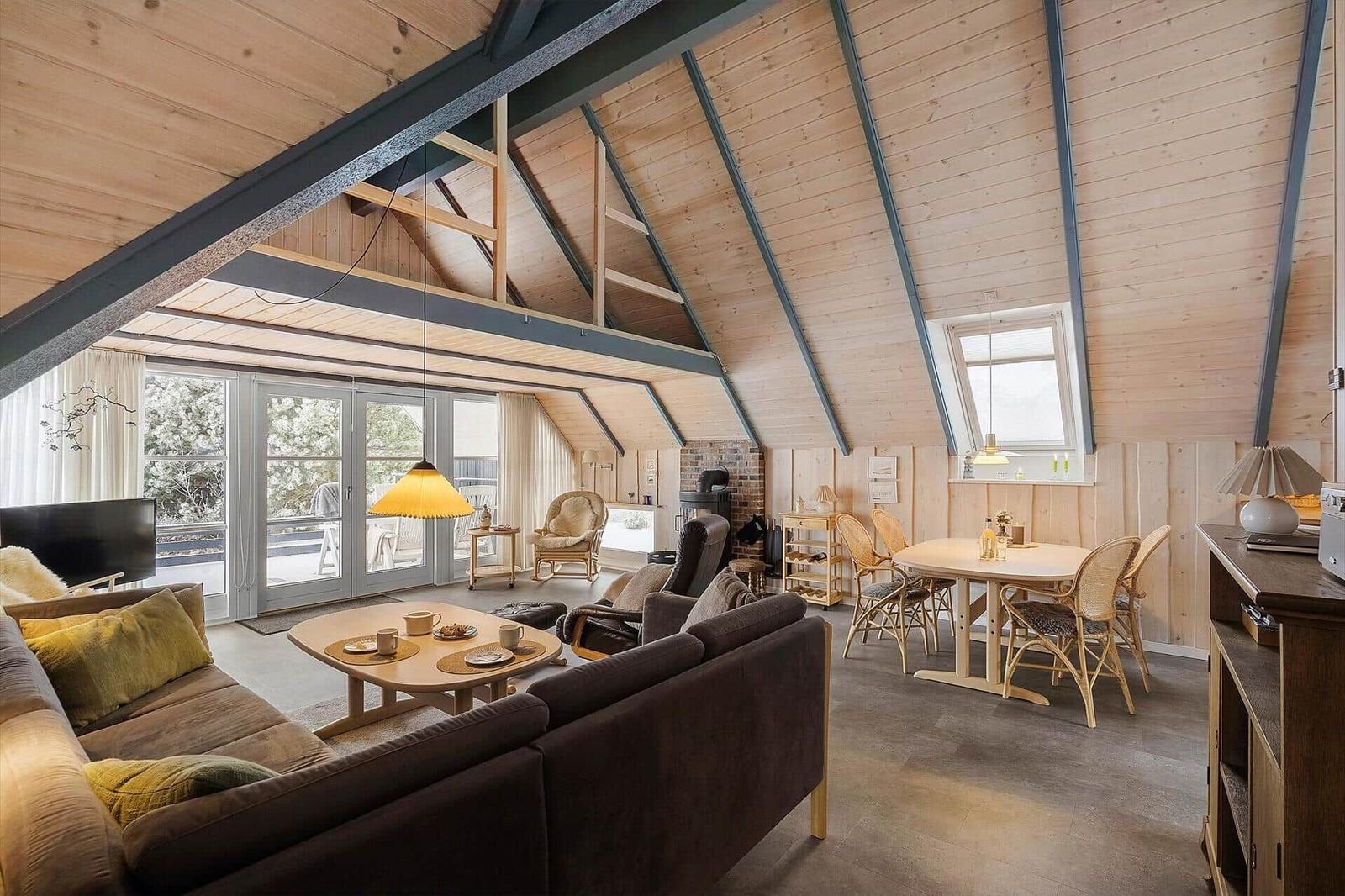 Wohn- und Essbereich mit Holzdecke, Sofa, Esstisch und Fenster zur Terrasse.