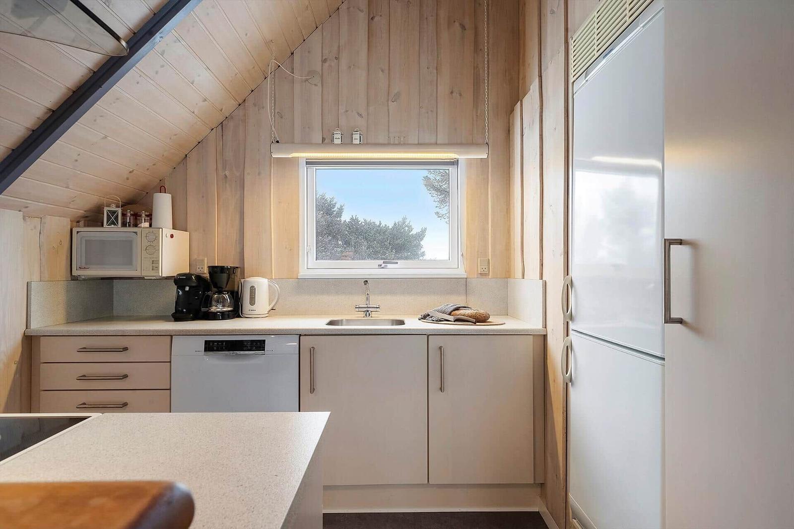 Küche mit Spüle, Kühlschrank und Fenster zum Blick auf Bäume.
