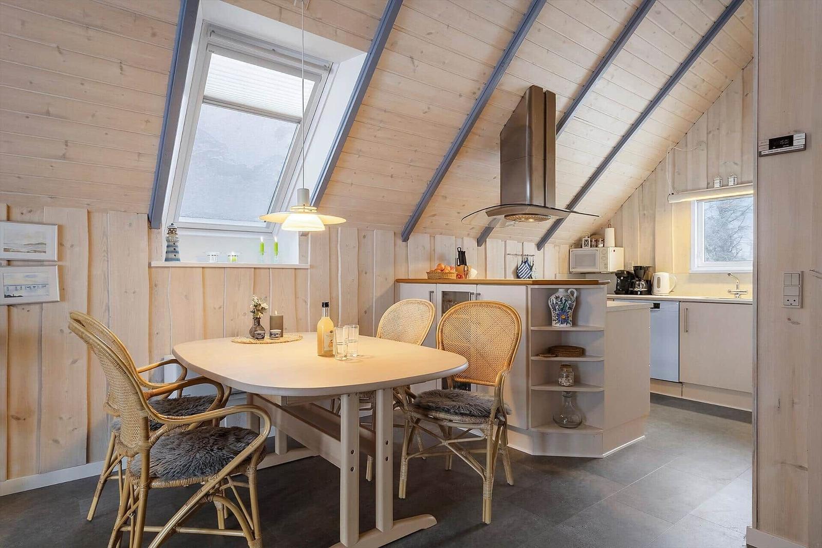 Essbereich mit Tisch und Stühlen unter Holzdach, Küchenzeile mit Dunstabzug.