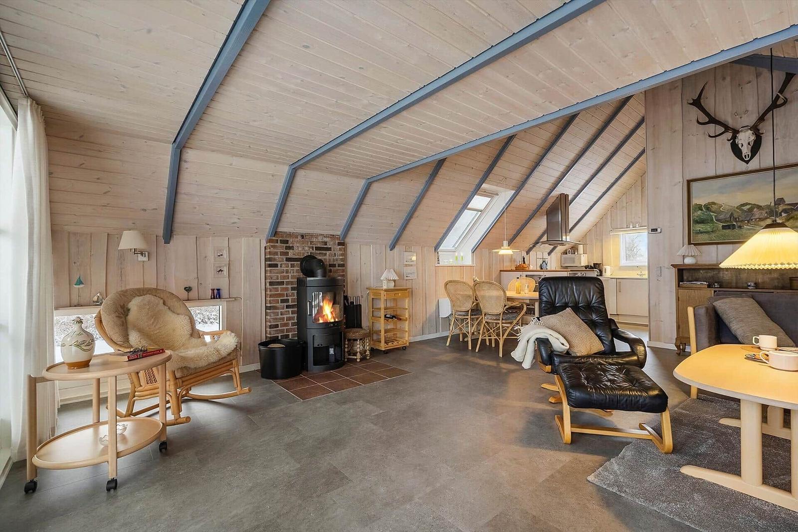 Wohn- und Essbereich mit Kamin, Sitzgelegenheiten und Küchenbereich unter Holzdecke.