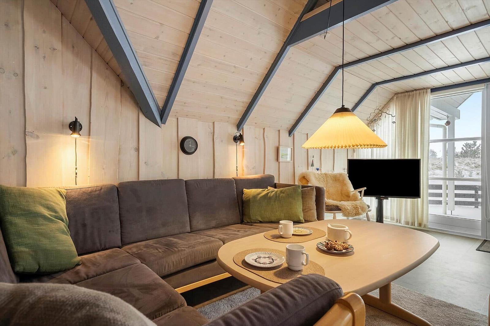 Ein Wohnzimmer mit Holzwand, Sofa, Tisch und Fernseher. Durchgang zum Balkon.