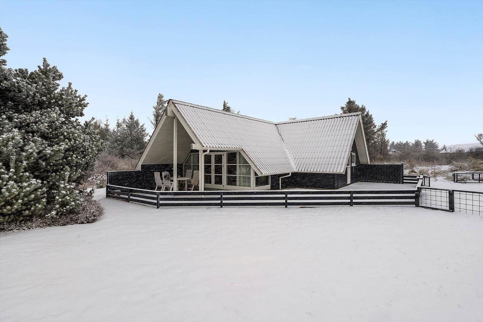 Wohnhaus mit schwarz-weißem Dach und Terrasse im Schnee.