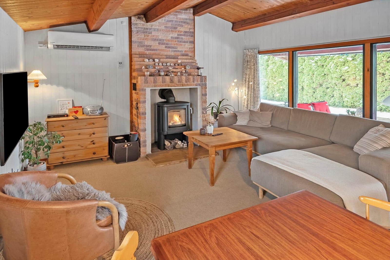 Living room with fireplace, sofa, and wooden furniture. Large windows and TV.