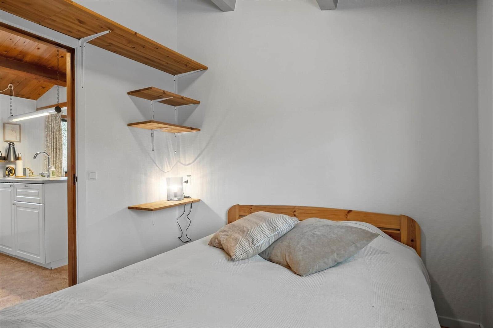 Bedroom with bed, wooden shelves, and view into the kitchen.