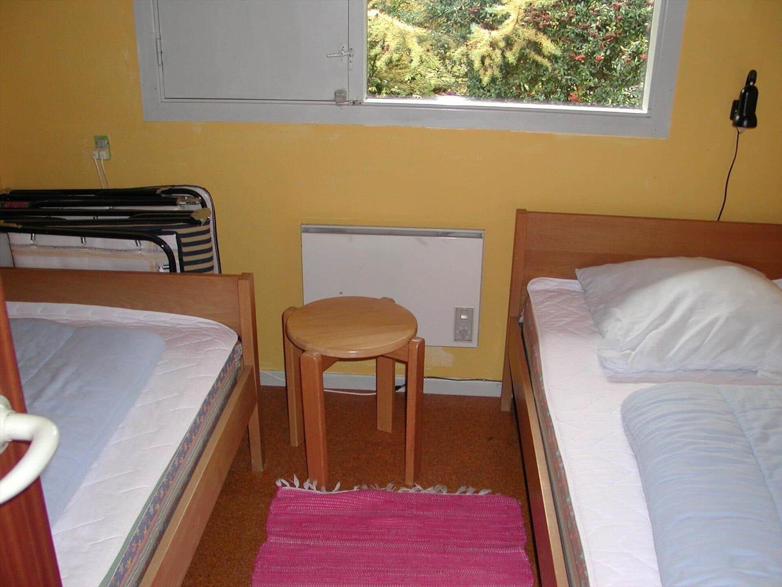 Two beds, small table, window with green view, wall heater, and pink rug.