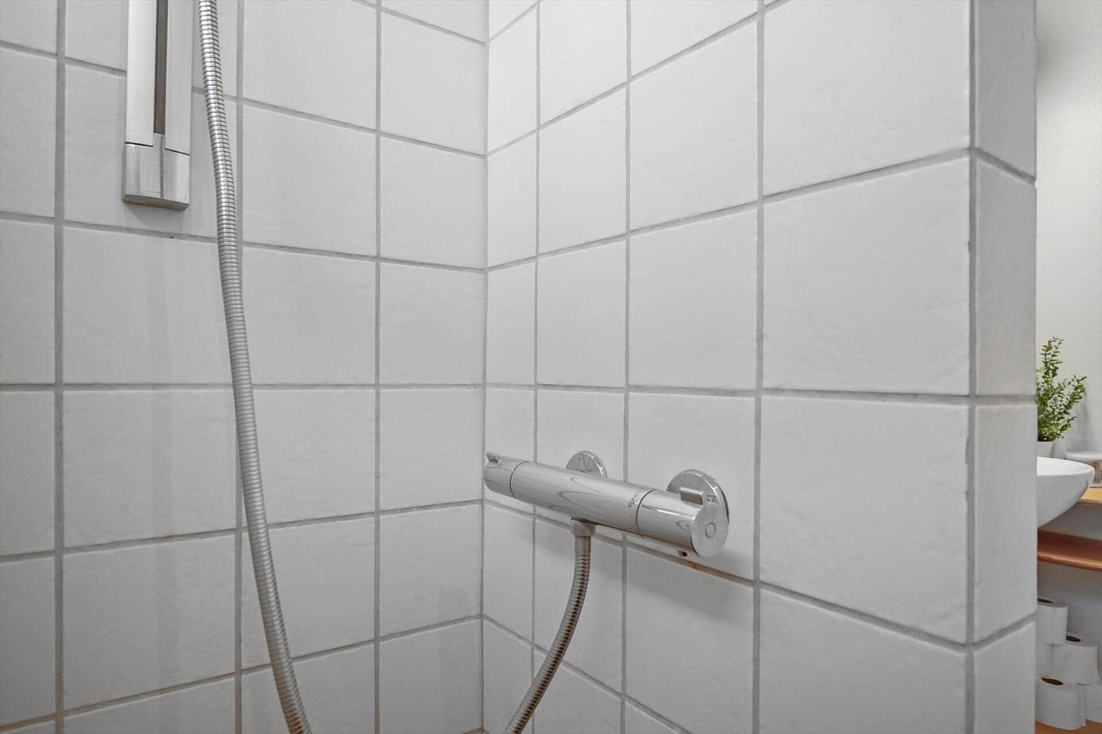 Shower with handheld showerhead and thermostatic mixer on white tiled wall