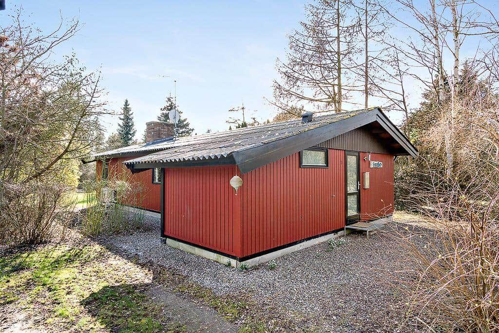 Red wooden house with roof and entrance door in the woods
