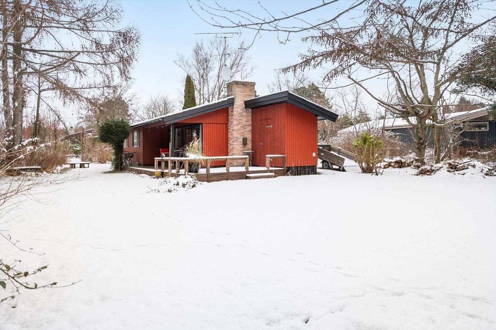 Red house with snow-covered grounds and wooden terrace in winter.