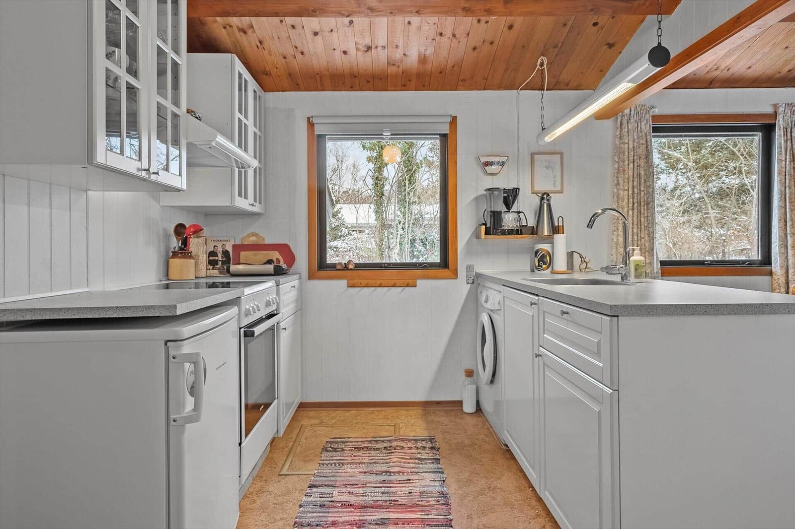 Kitchen with white cabinets, wood ceiling, and windows overlooking snow.