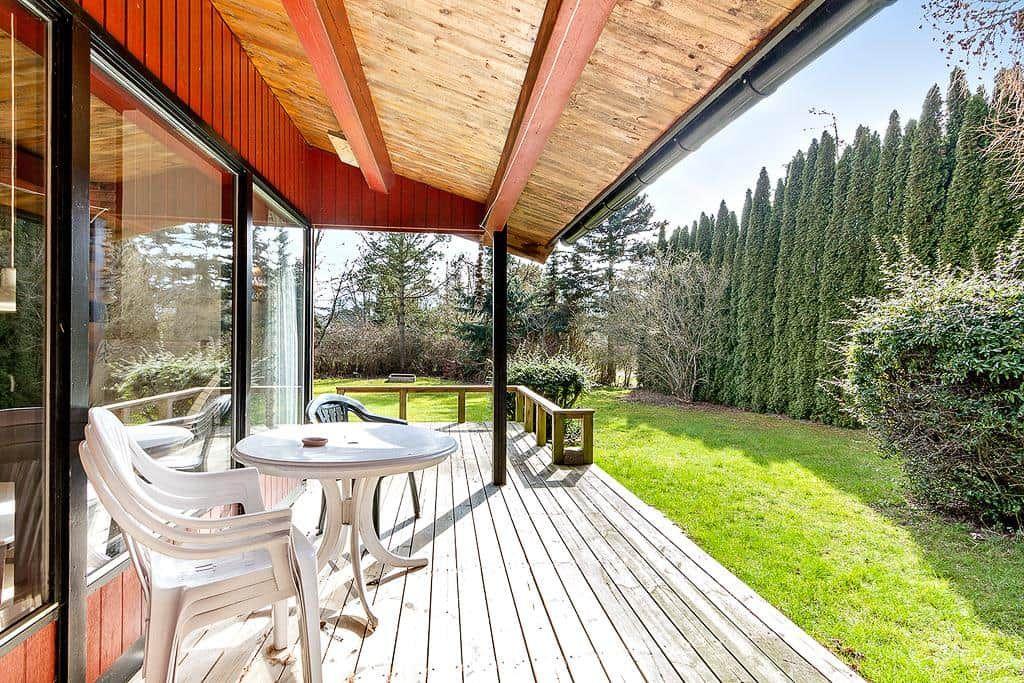 Deck with table and chairs, view of green lawn and trees.