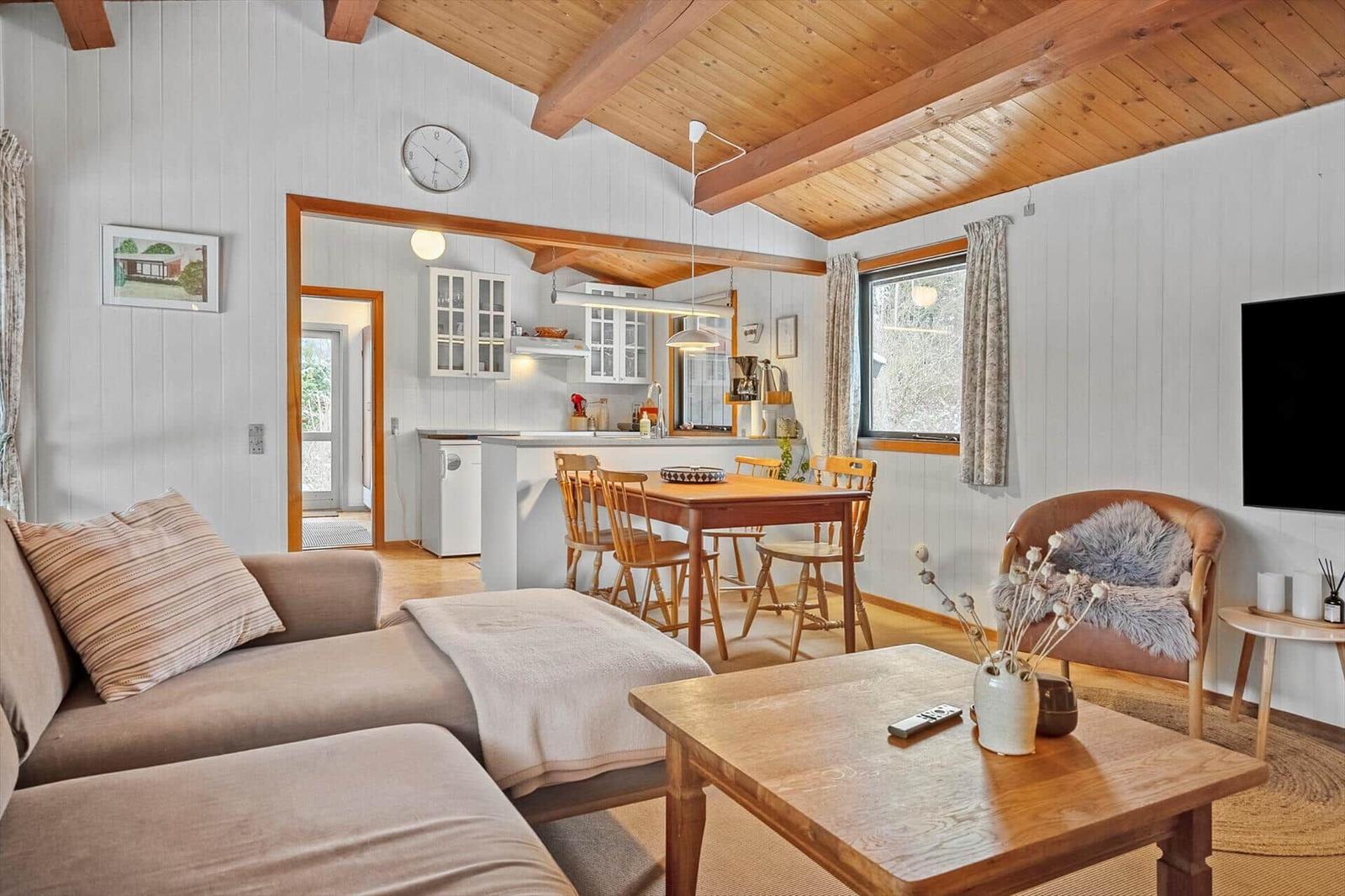 Living room with dining area and kitchen. Wooden ceiling, sofa, dining table, and TV.