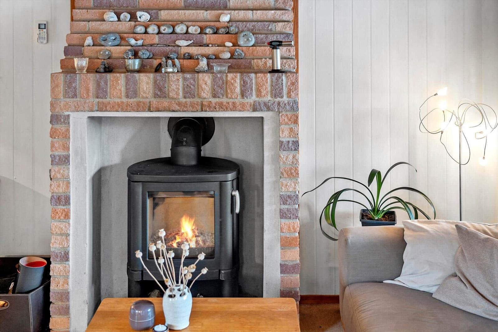 A fireplace with a wood stove, decorative stones, and plants in the living area.