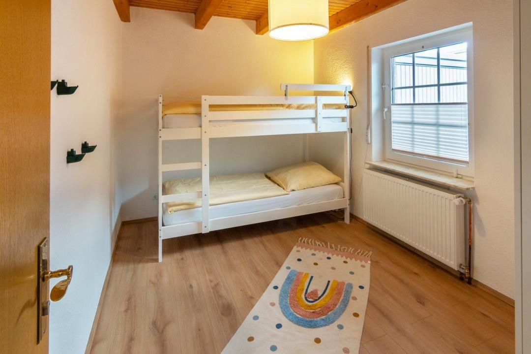 Room with bunk bed, window, and wooden floor.