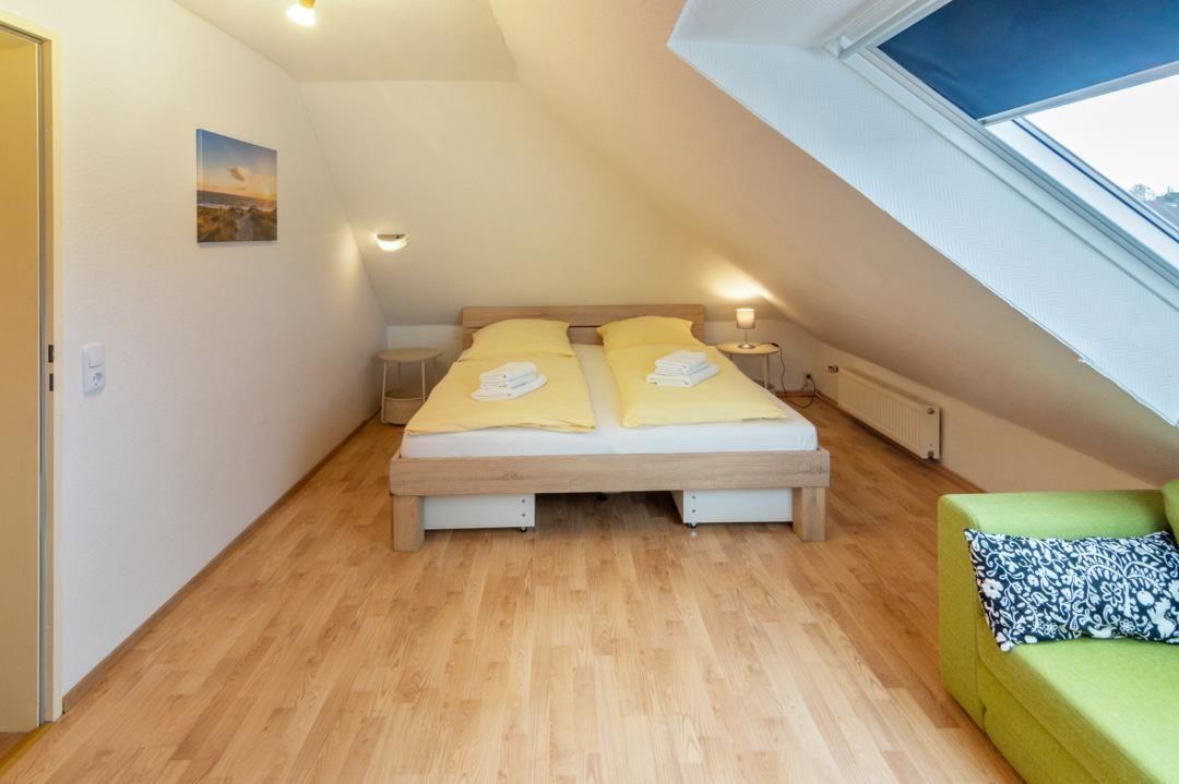 Bedroom with sloped ceiling, bed, sofa, and skylight.