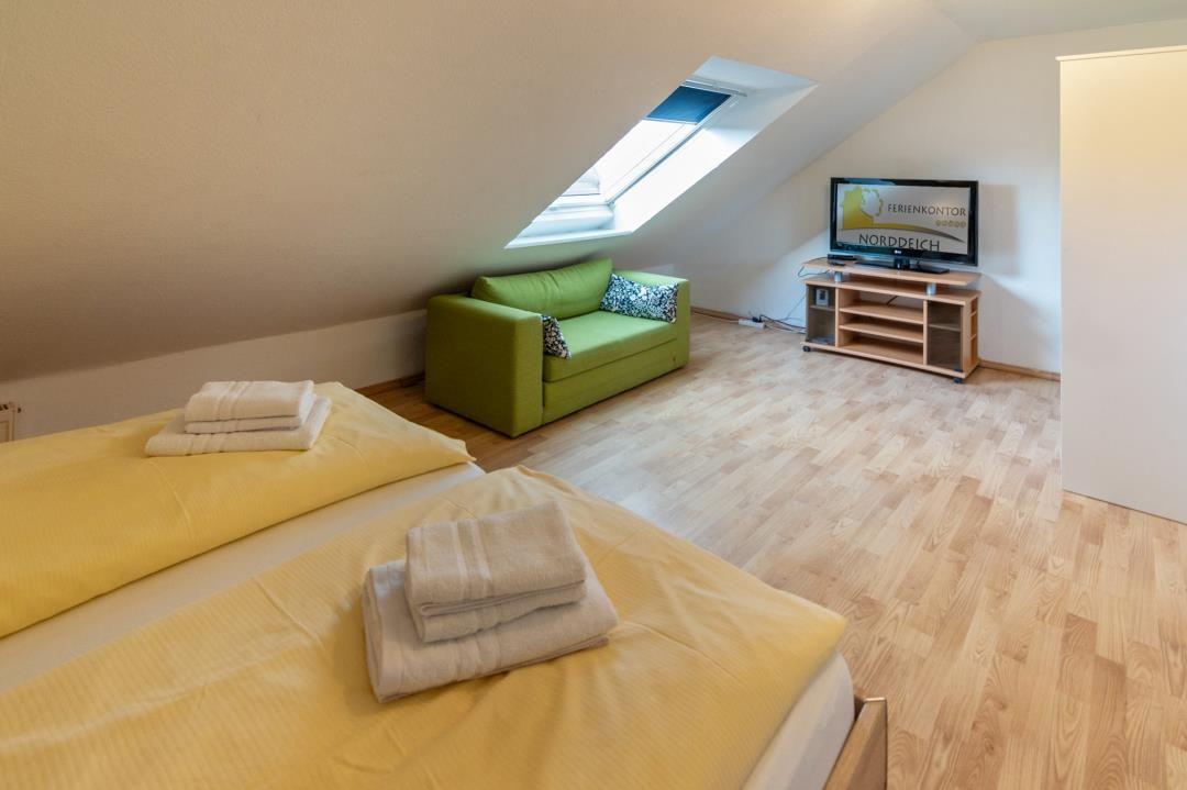 Bedroom with sloped ceiling, green sofa, and TV.