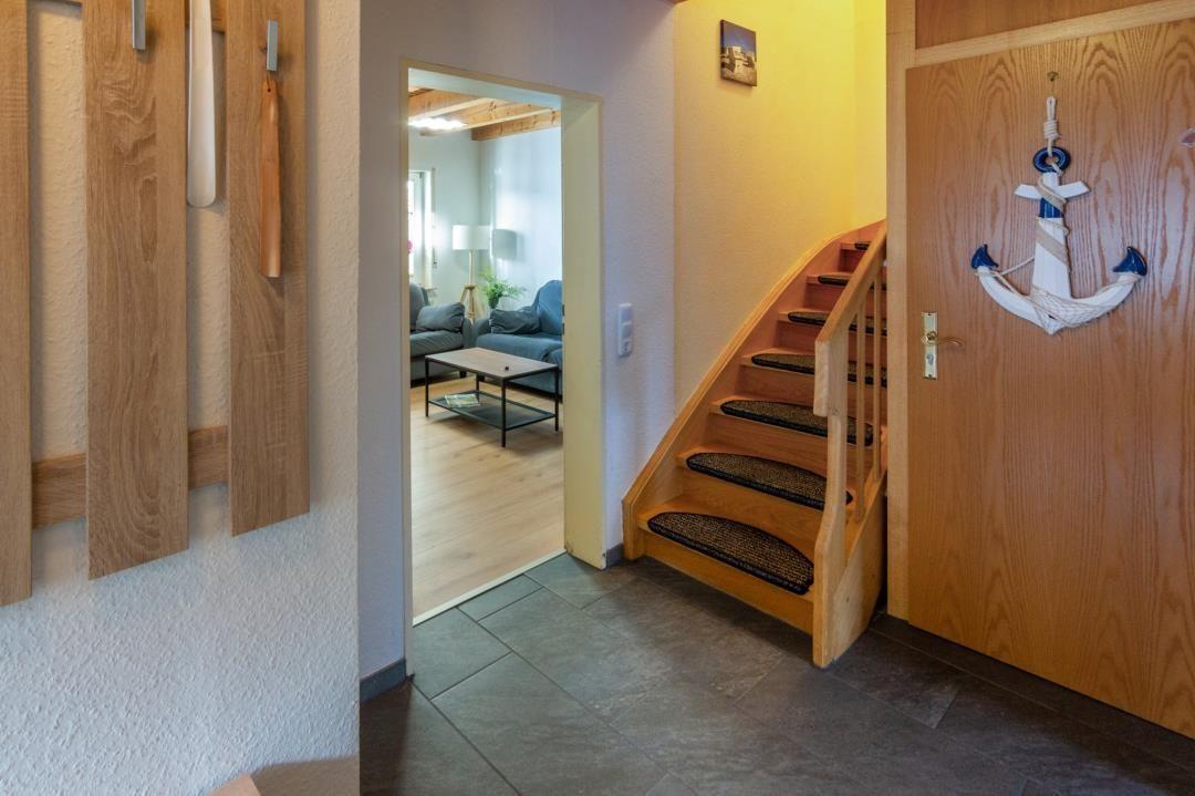 Entrance with wooden stairs and door with anchor decor. View into living room with sofa and table.