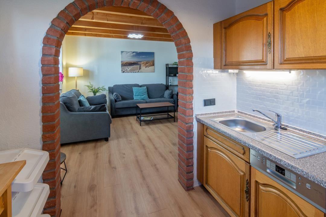 Kitchen with wooden cabinets and view into living room through brick arch.