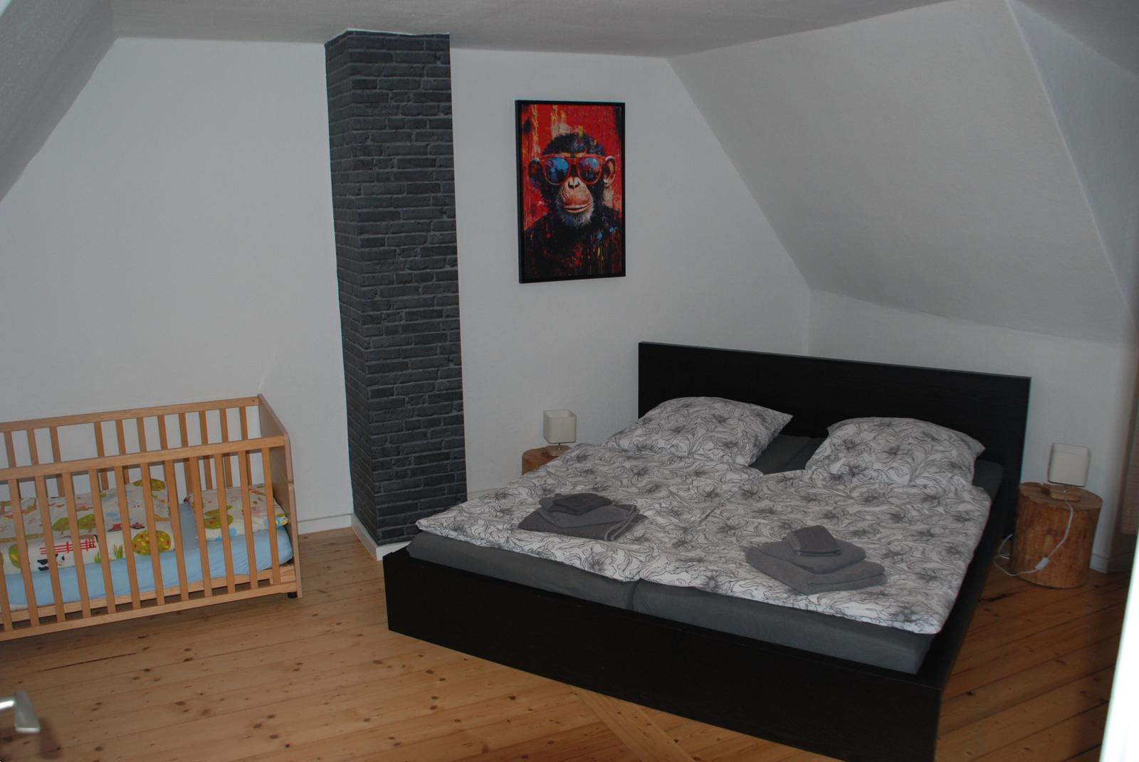 Schlafzimmer mit Babybett, Bett und Wandbild
