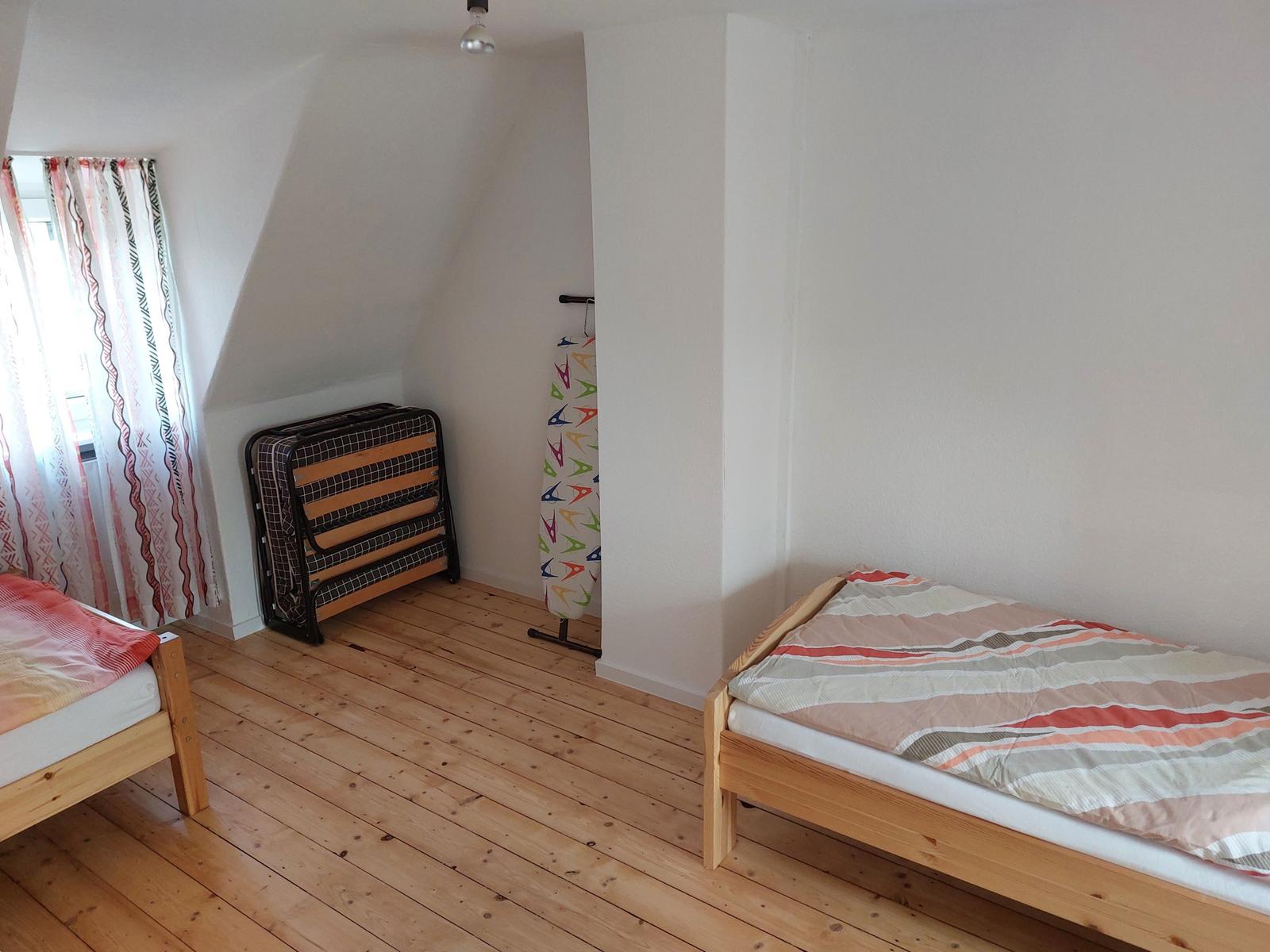 Zwei Einzelbetten, Holzboden, Fenster mit Vorhängen, Klappbett und Bügelbrett.