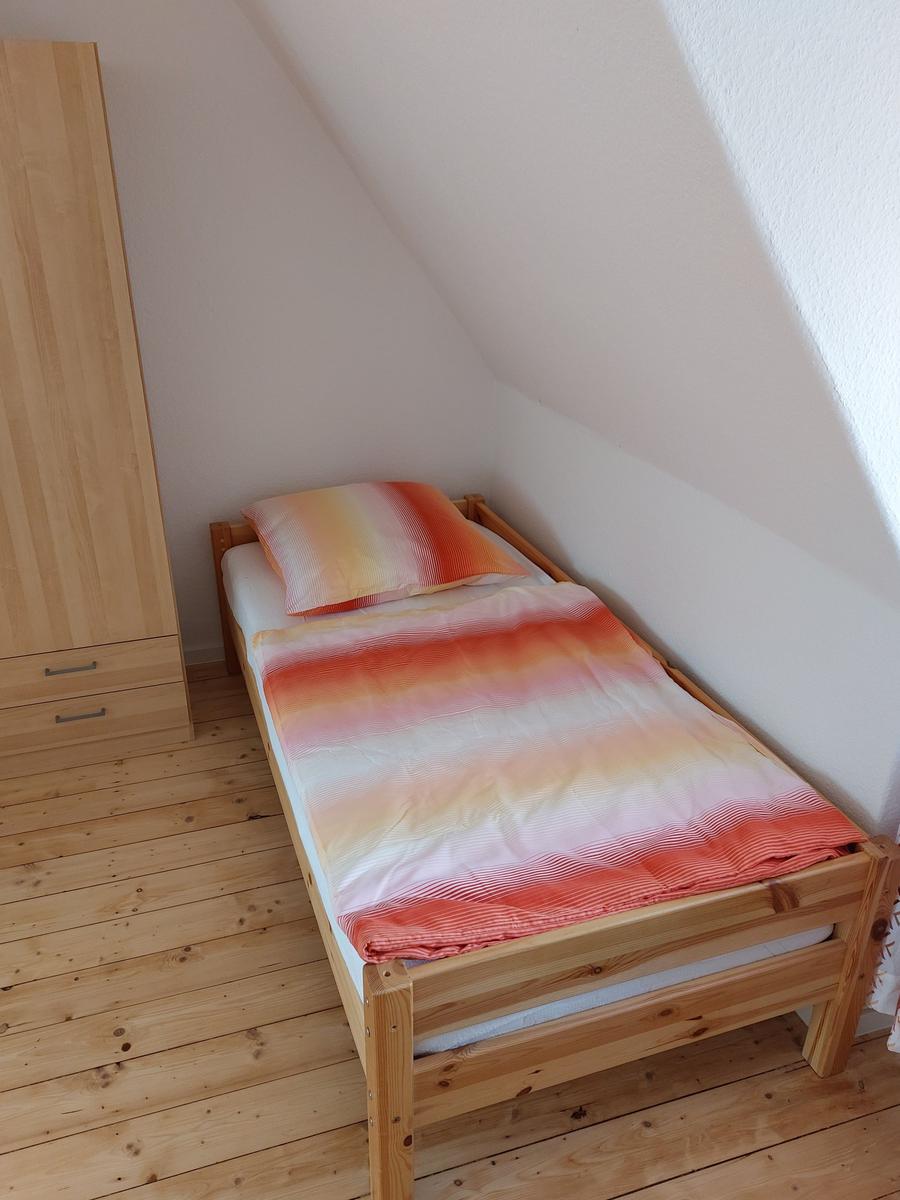 Ein Schlafzimmer mit Dachschräge, Holzboden und einem Bett mit orangefarbenem Bettzeug.