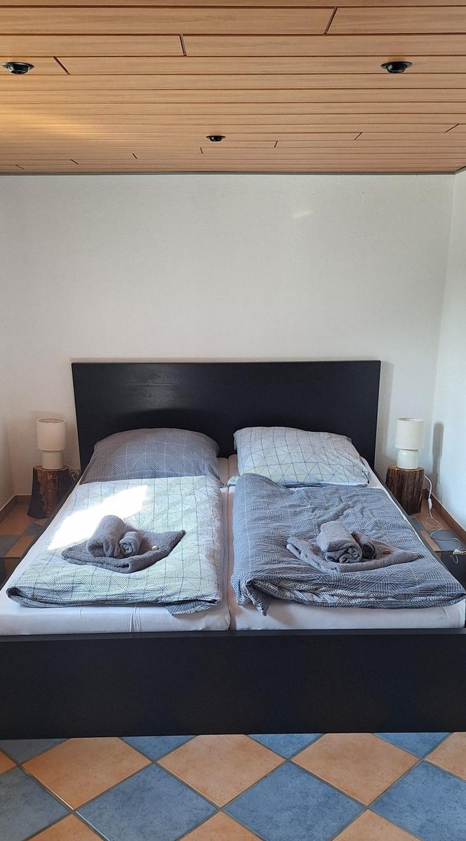 Schlafzimmer mit Doppelbett, Holzdecke und gefliestem Boden. Beide Seiten mit Bettwäsche und Handtüchern.