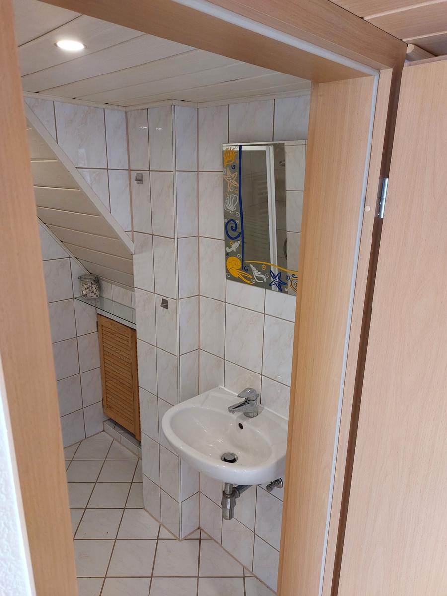 Badezimmer mit Waschbecken, Spiegel und Dusche unter Dachschrägen.