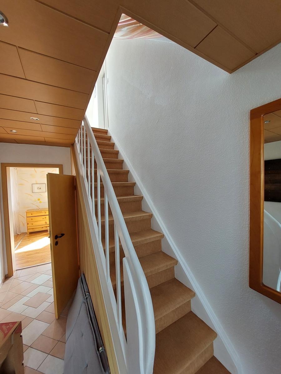 Treppe mit Teppichstufen führt nach oben. Holzdecke und Wandspiegel sichtbar.