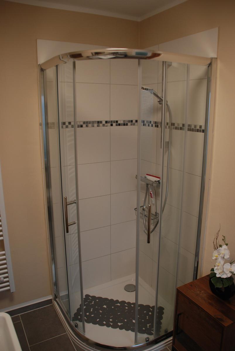 Duschkabine mit Glaswand, weißen Fliesen und Mosaikstreifen an der Wand.