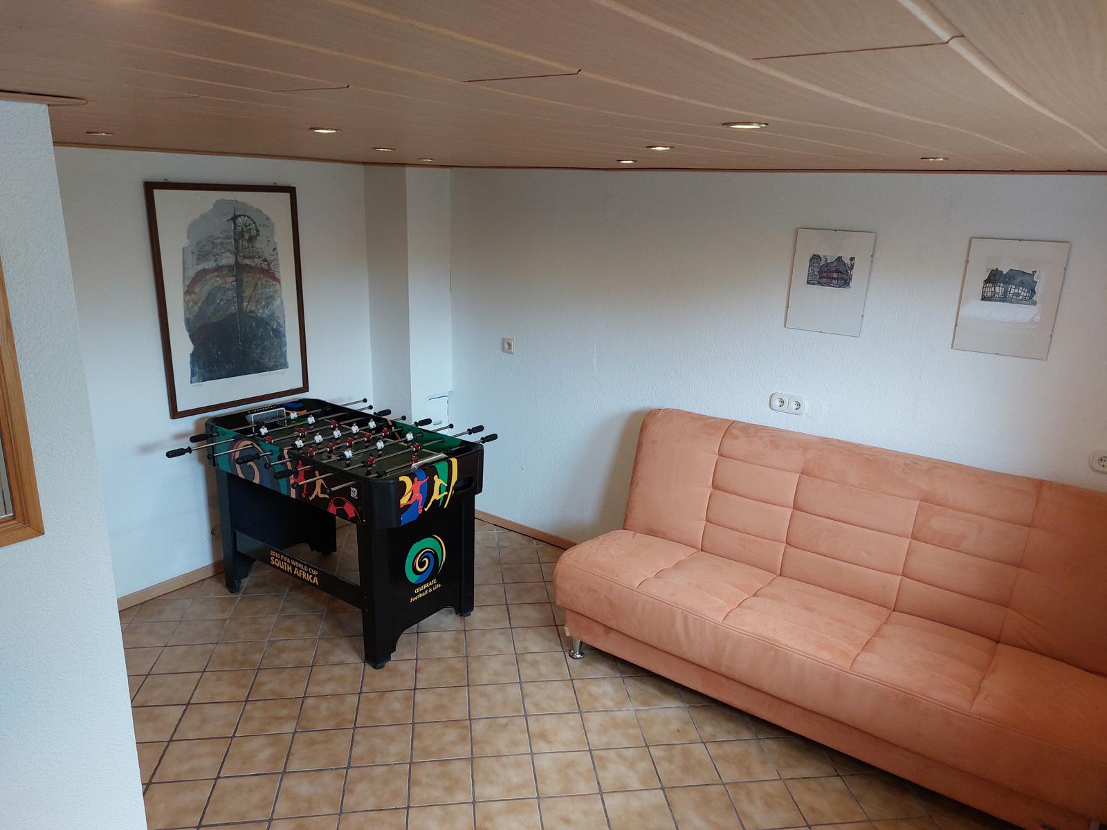 Raum mit Sofa und Tischfußball, Wandbilder und gefliestem Boden.