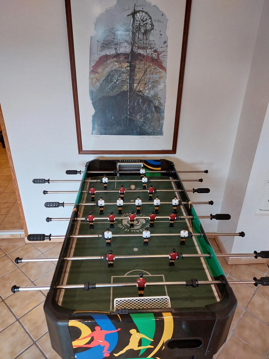 Fussballtisch mit Spielern und Tor. Wandbild darüber. Fliesenboden.