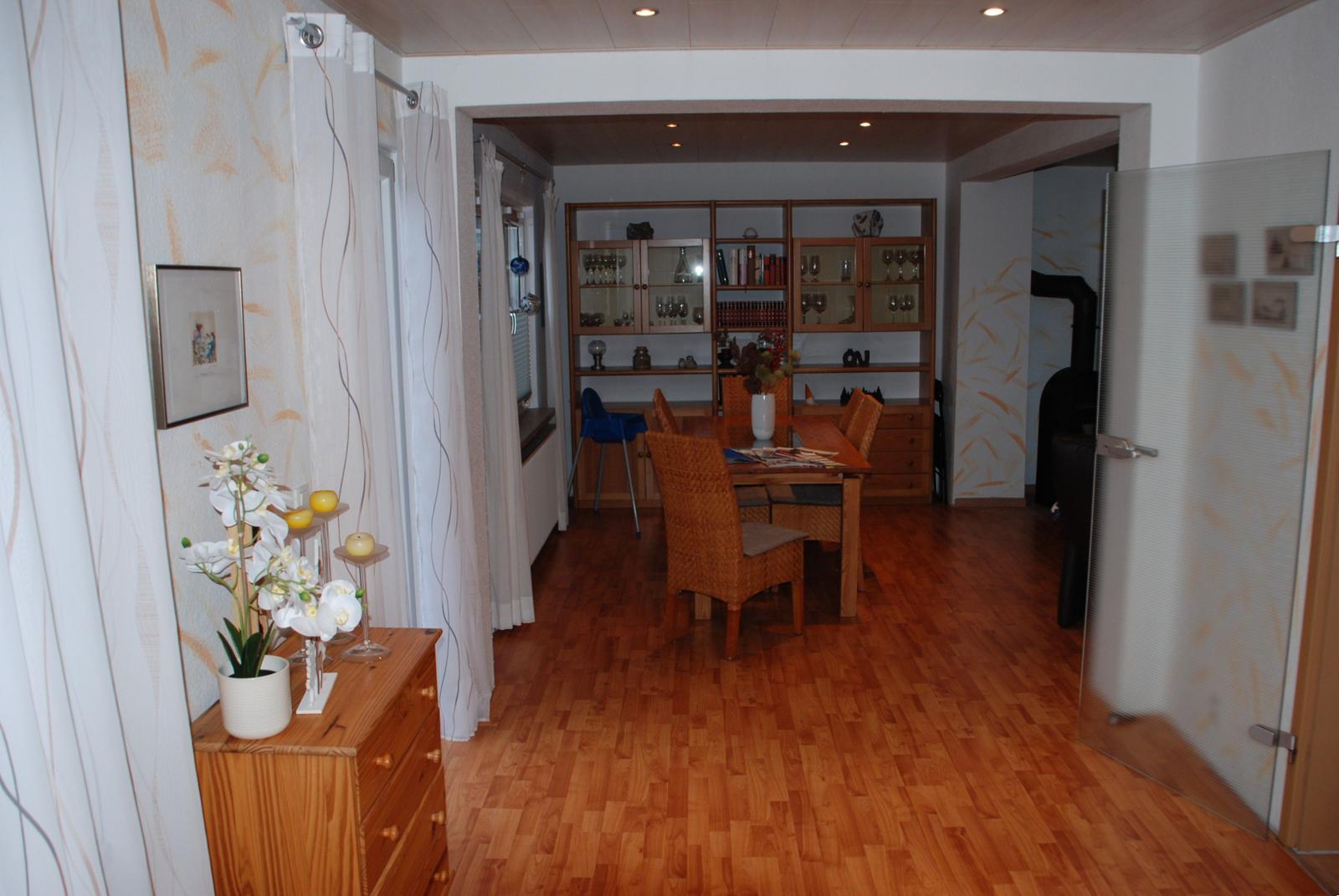 Ein Esszimmer mit Holzboden, Tisch, Stühlen und einer Glasvitrine im Hintergrund.