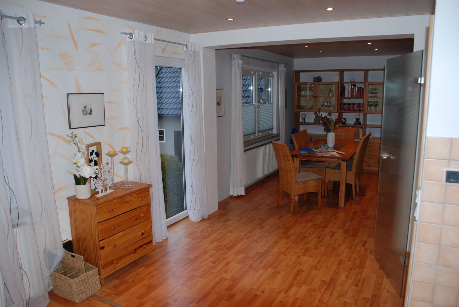 Wohn- und Essbereich mit Holzboden, Tisch, Stühlen und Schrank im Hintergrund.