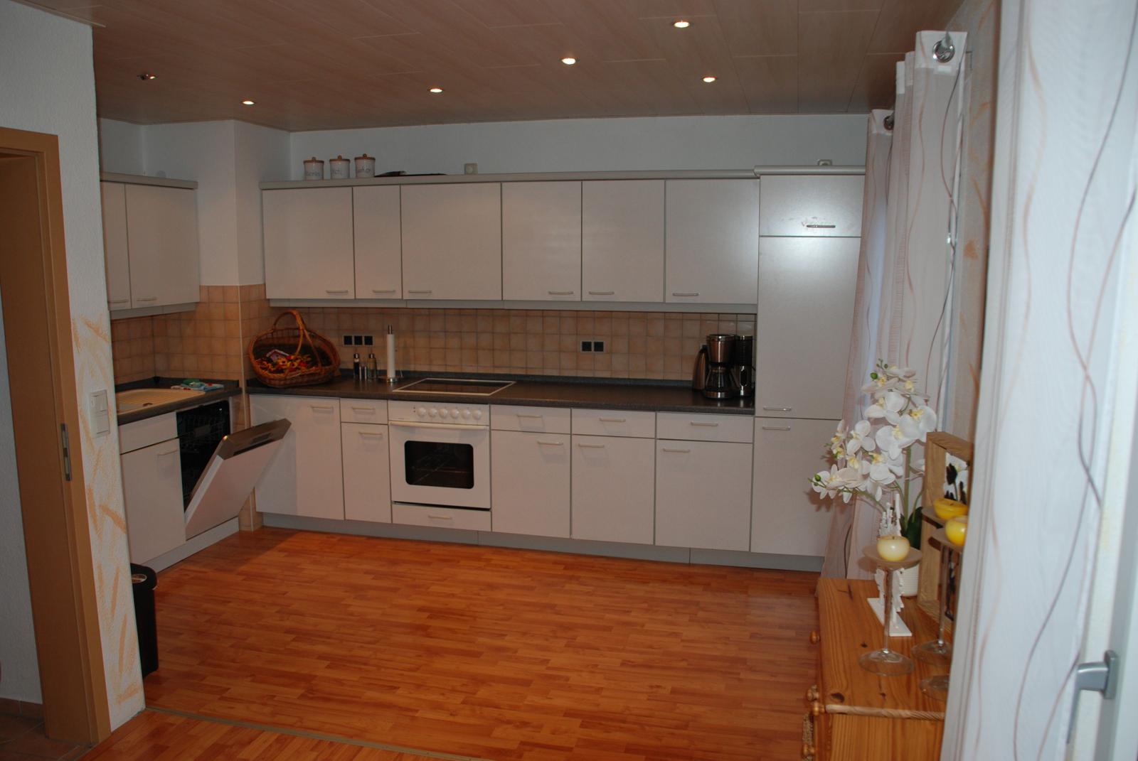 Küche mit weißen Schränken, Holzboden und Edelstahlgeräten.