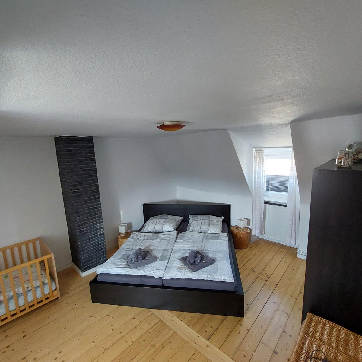 Schlafzimmer mit Doppelbett, Kinderbett und Holzboden.