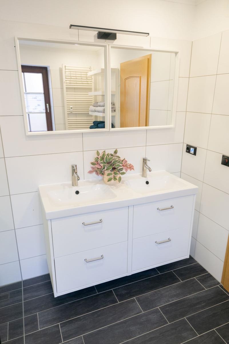 Modernes Badezimmer der Ferienwohnung Bergmoment in Blankenburg Harz mit Doppelwaschtisch, Dusche, Fenster und Handtuchheizkoerper.