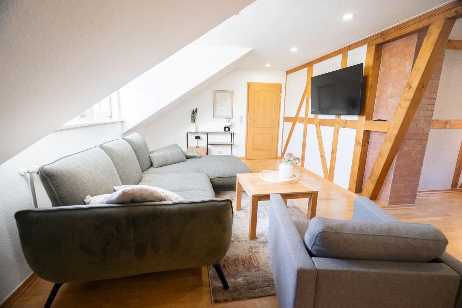 Modernes Wohnzimmer der Ferienwohnung Bergmoment in Blankenburg Harz mit Sofa, Dachschraege und offenem Wohnkonzept.