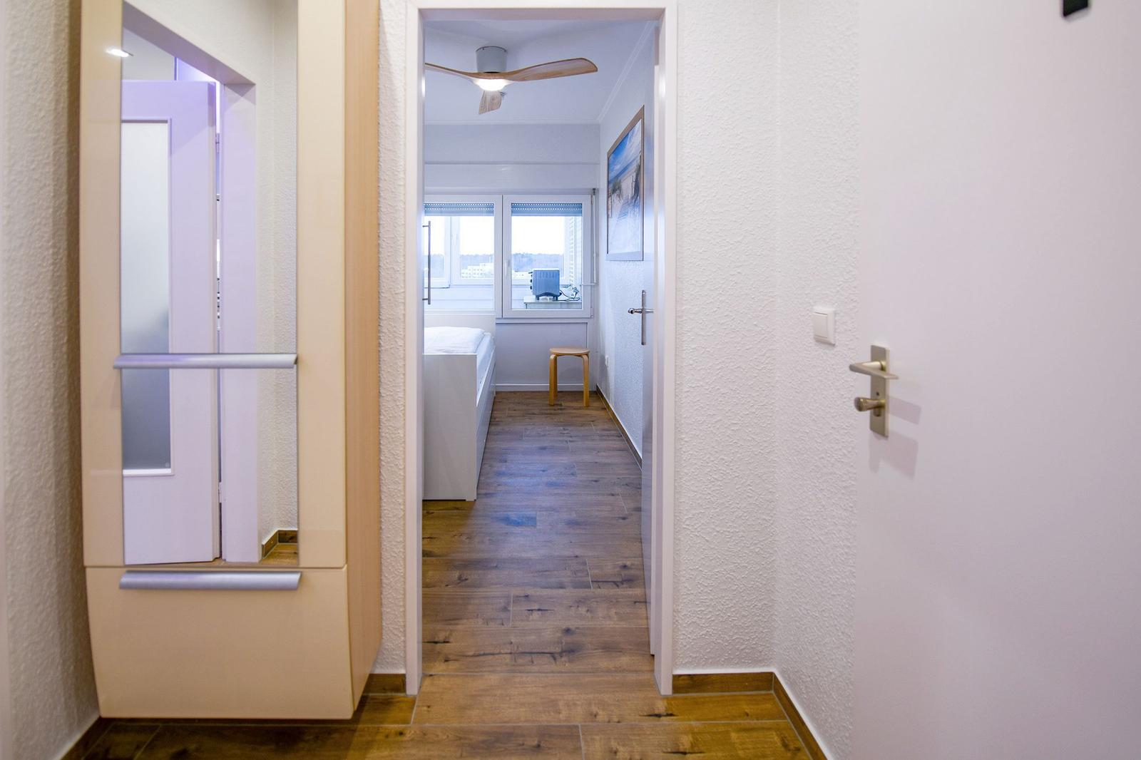 Flur mit Holzboden führt in Schlafzimmer mit Bett und Fenster.