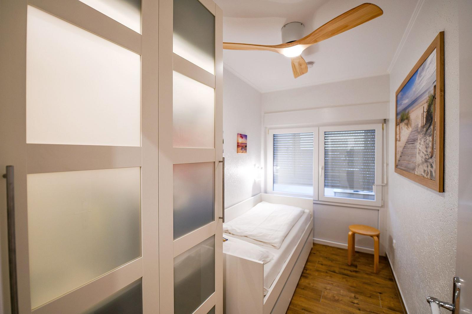 Schlafzimmer mit Bett, Fenster, Stuhl und Deckenventilator.