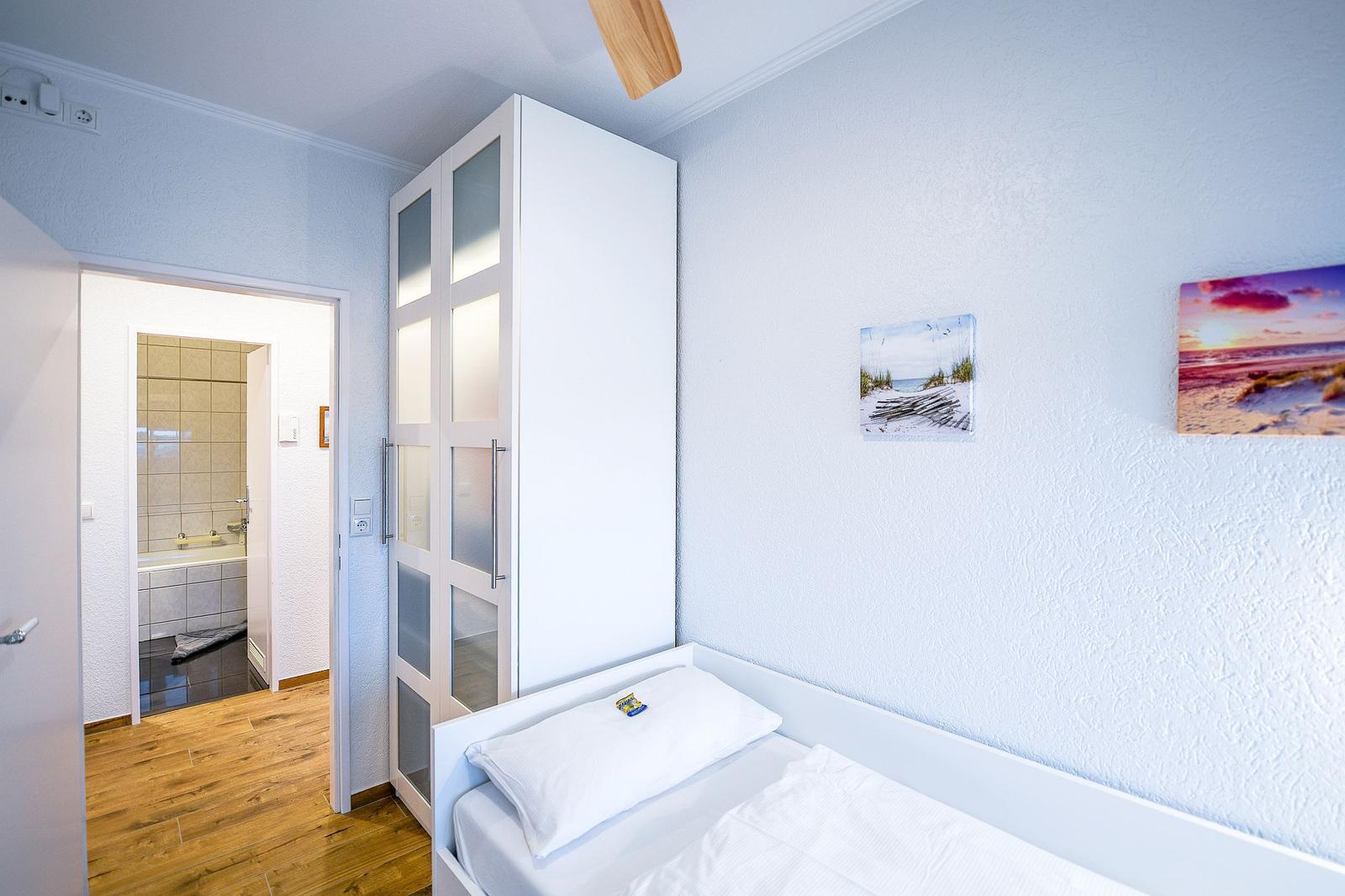 Schlafzimmer mit Bett, Kleiderschrank und Bad im Hintergrund.