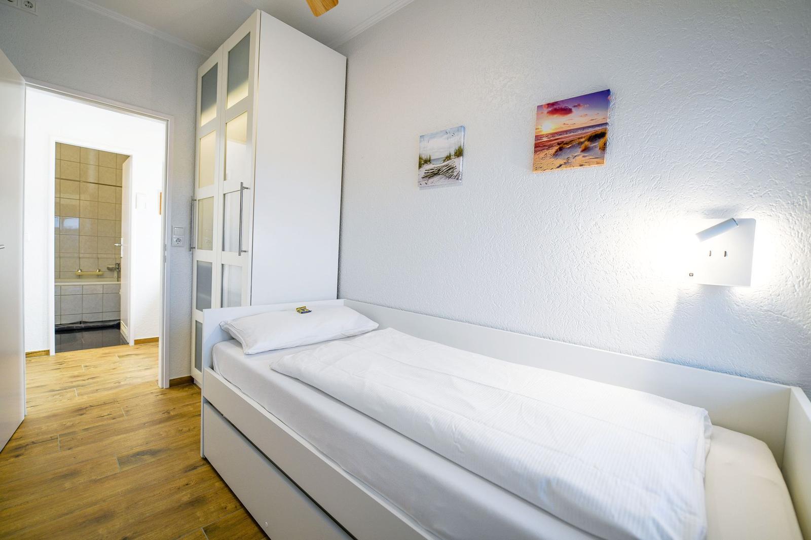 Schlafzimmer mit Bett, Kleiderschrank und Bad im Hintergrund.