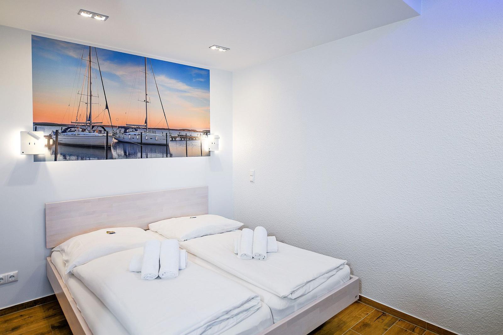Schlafzimmer mit Doppelbett und Wandbild von Segelyachten.