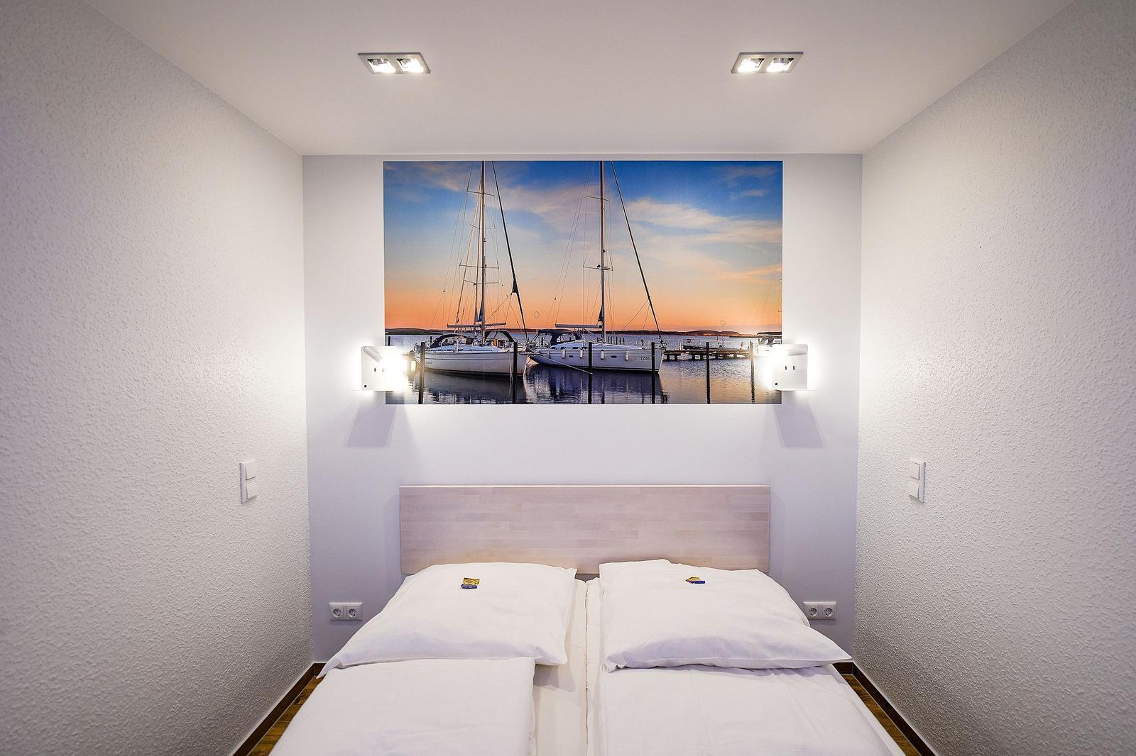 Schlafzimmer mit Bett und Wandbild von Segelbooten.