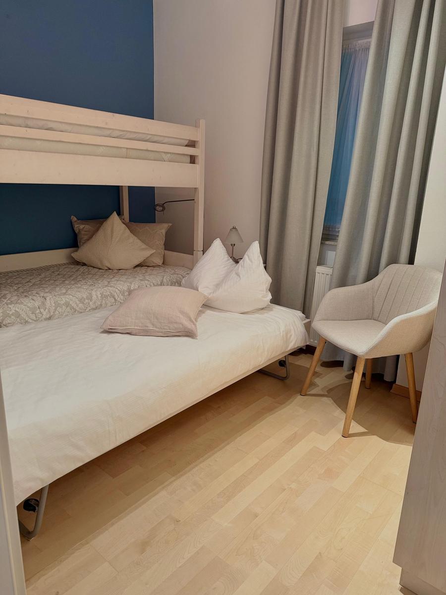 Ein Schlafzimmer mit Doppelbett, Stuhl und Fenster mit Vorhängen.