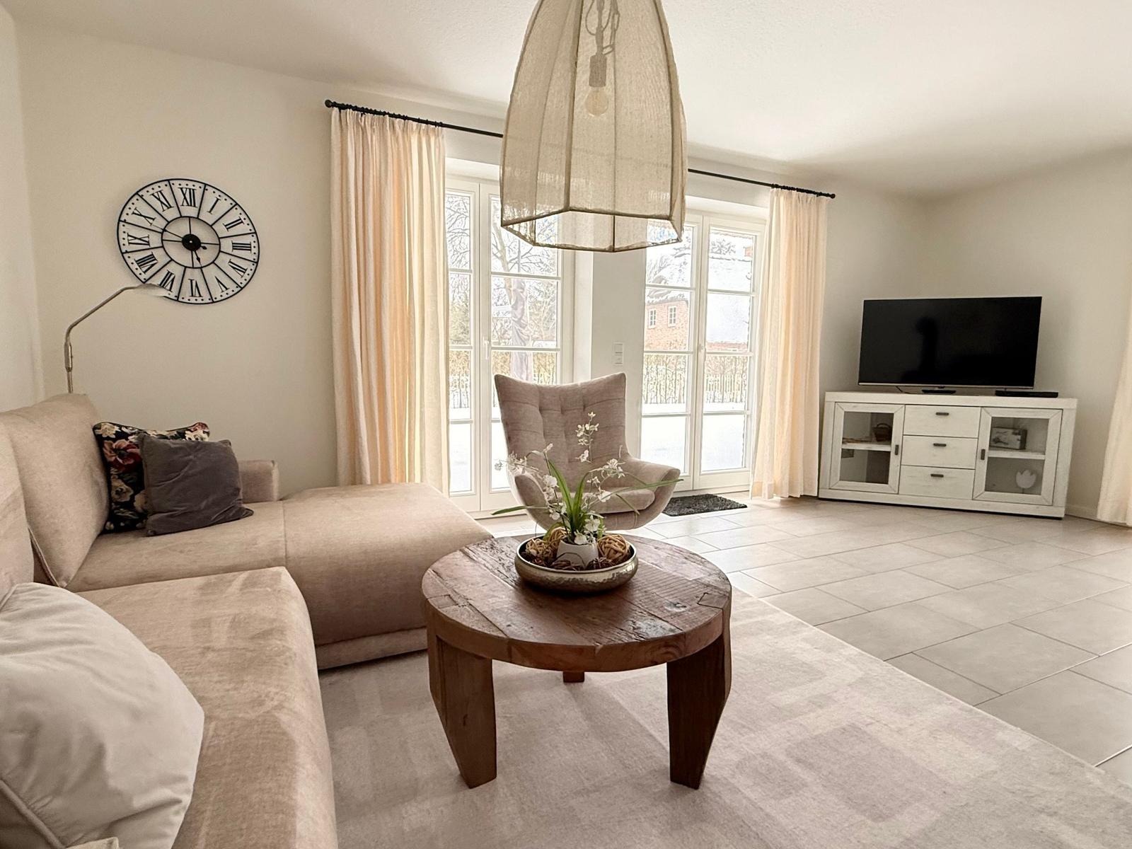 Wohnzimmer mit Sofa, TV und Glastüren zum Garten.