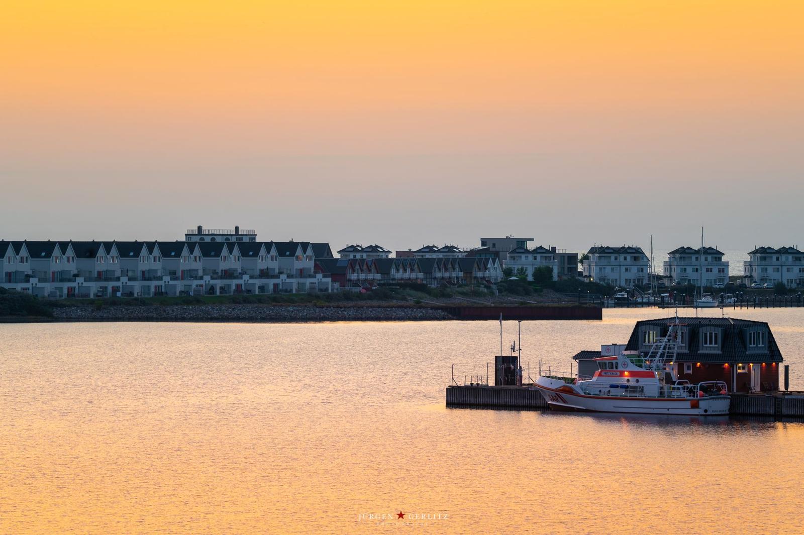 Sonnenuntergang über Wasser mit Boot und Häusern im Hintergrund.