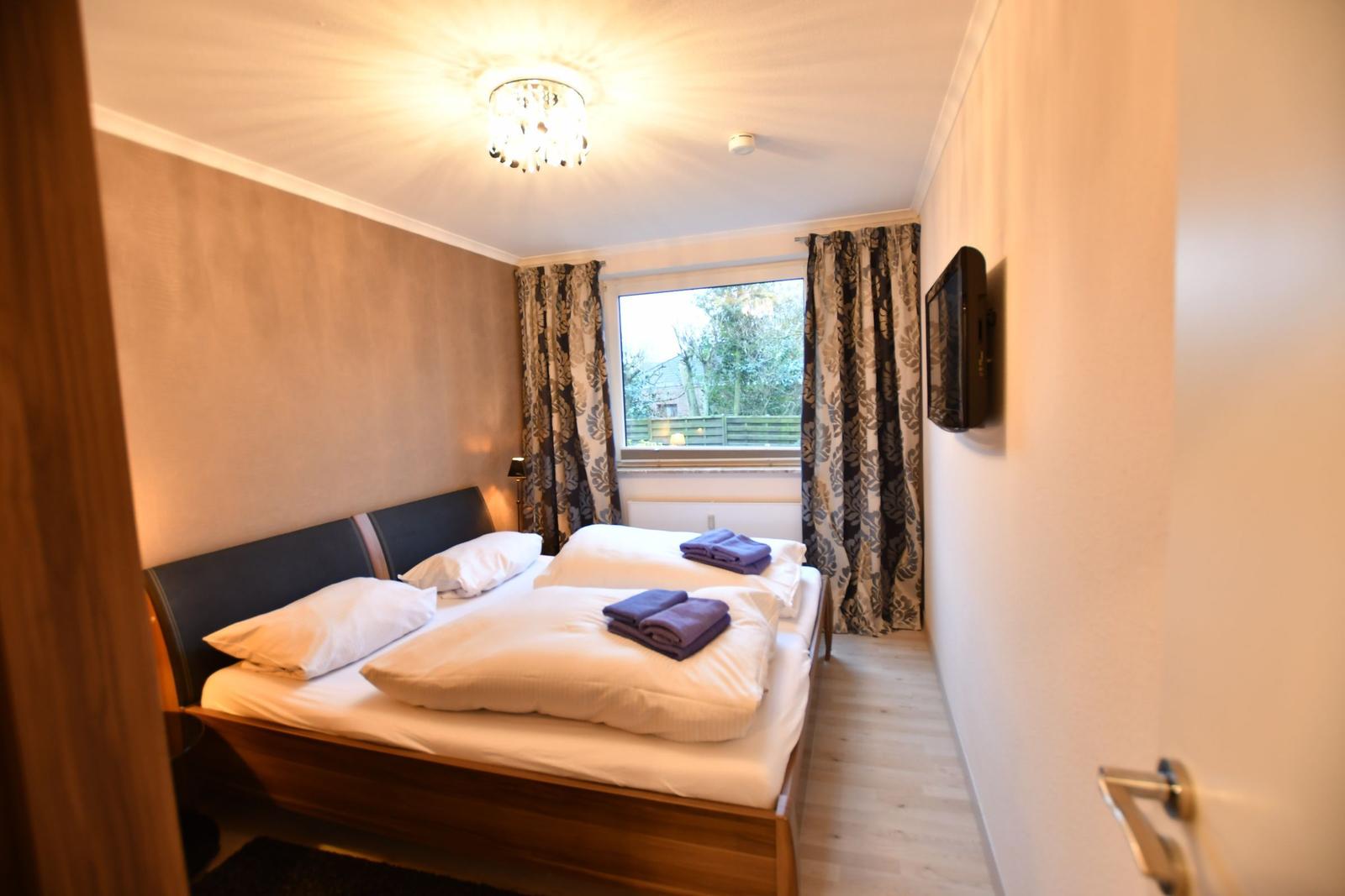 Schlafzimmer mit Doppelbett, Fenster und TV.