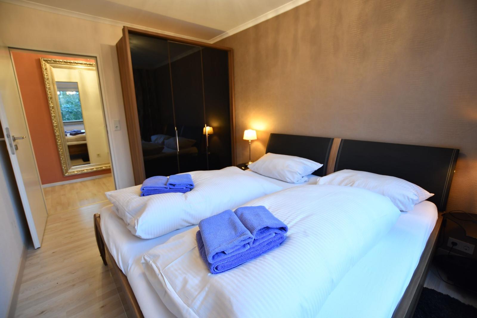 Schlafzimmer mit Doppelbett, blauen Handtüchern und Spiegelschrank.