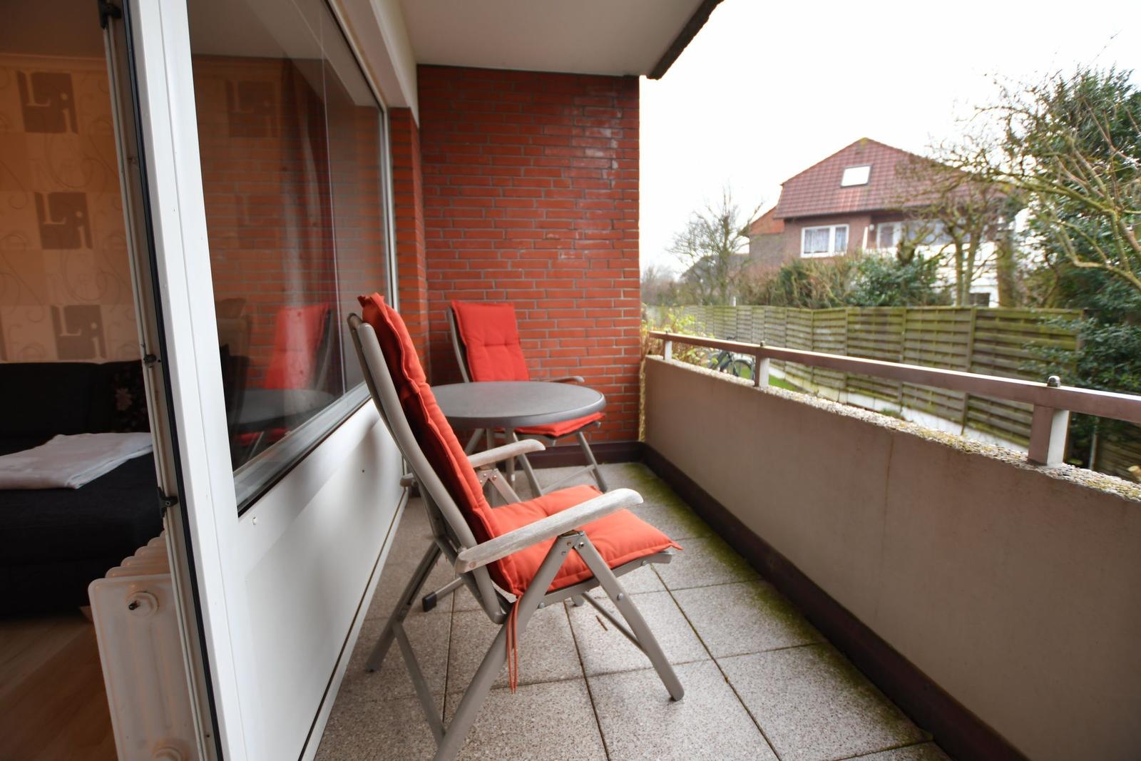 Terrasse mit zwei Stühlen und Tisch, rote Kissen, Blick auf Nachbarhaus.